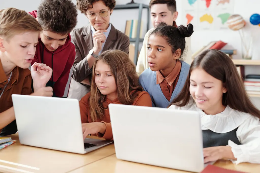 Students and a teacher gathered around laptops in a classroom.