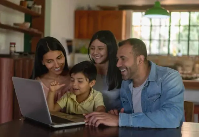 A family gathered around a laptop together at home.